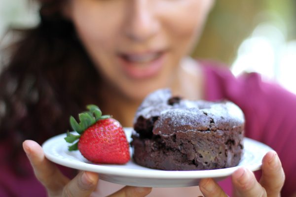 Woman looking at a plate carrying a strawberry and brownie