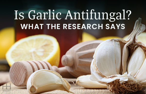 Cloves of garlic on a wooden table next to a lemon and cooking utensils.