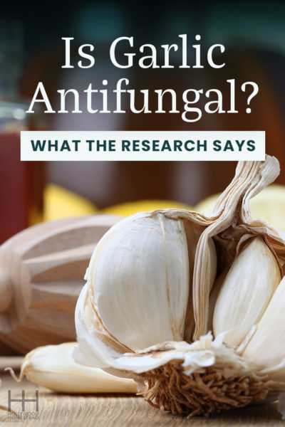 Cloves of garlic on a wooden table next to a lemon and cooking utensils.