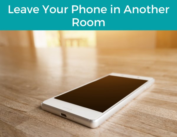 smartphone on a wooden table under the title "Leave Your Phone in Another Room"